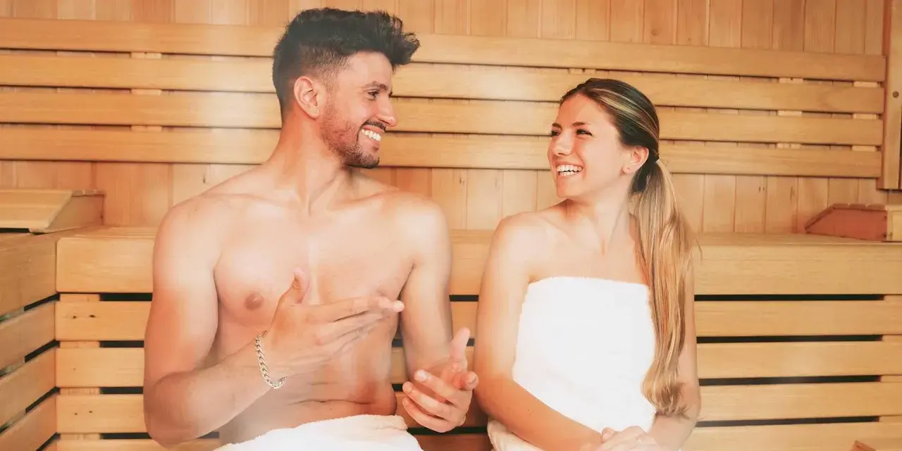 Coppia sorridente in una sauna di legno, un rituale di benessere quotidiano.