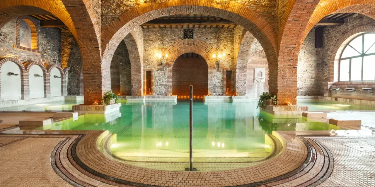 Un suggestivo thermarium, con vasche termali verdi sotto archi in mattoni e pietra, evoca un'atmosfera di antico benessere.