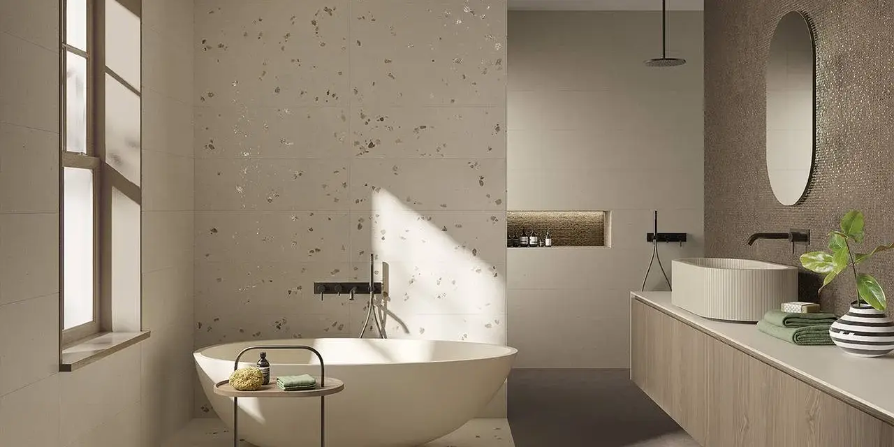 Bagno moderno con vasca freestanding e lavabo su mobile in legno. Il pavimento fap, con le sue venature chiare e inclusioni dorate, riflette la luce naturale.