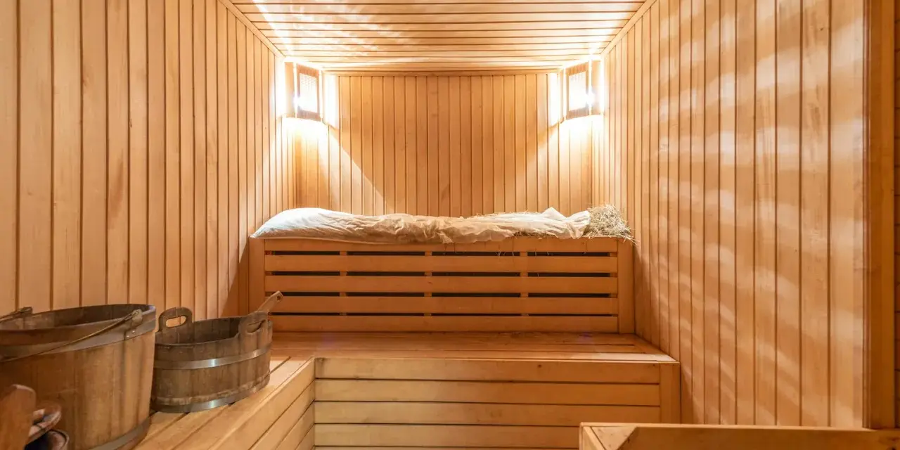 Interno di una sauna norvegese in legno, con panche, secchi e luci soffuse.
