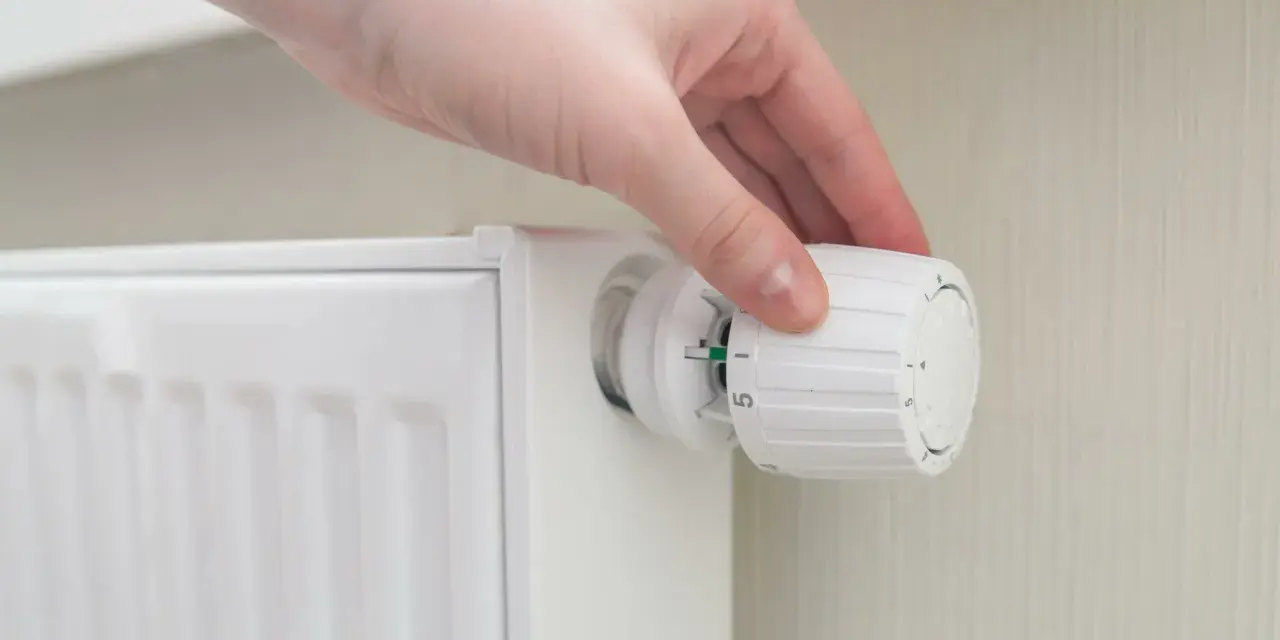 Mano che regola la manopola di un termosifone per ottimizzare la potenza.