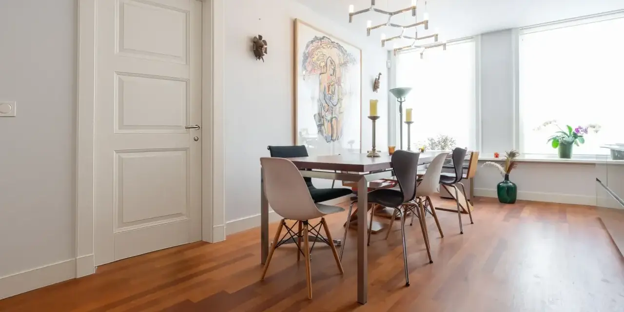 Un elegante soggiorno con parquet doussié e arredamento moderno. Tavolo da pranzo con sedie di design, quadro astratto e lampadario geometrico.