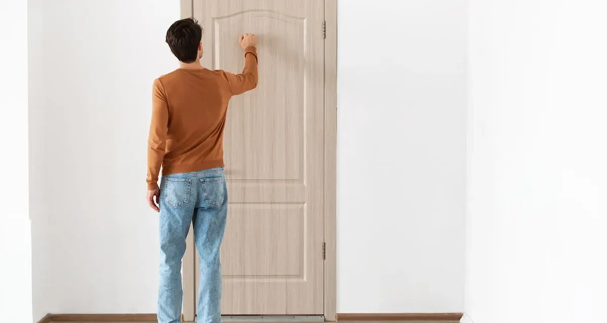 Uomo con maglione arancione e jeans bussa alla porta, forse per alzare la porta per posa pavimento.