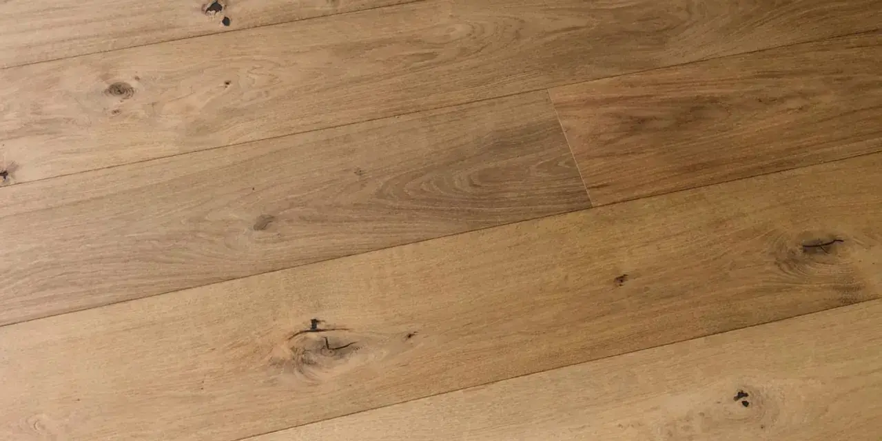 Dettaglio di assi di parquet prefinito in legno chiaro con nodi evidenti. Lo spessore del legno conferisce robustezza.