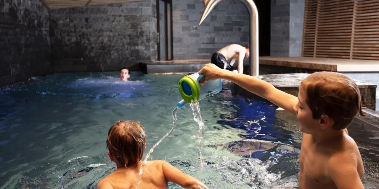 Bambini giocano in piscina, con un annaffiatoio. Nessuna indicazione su sauna età minima.