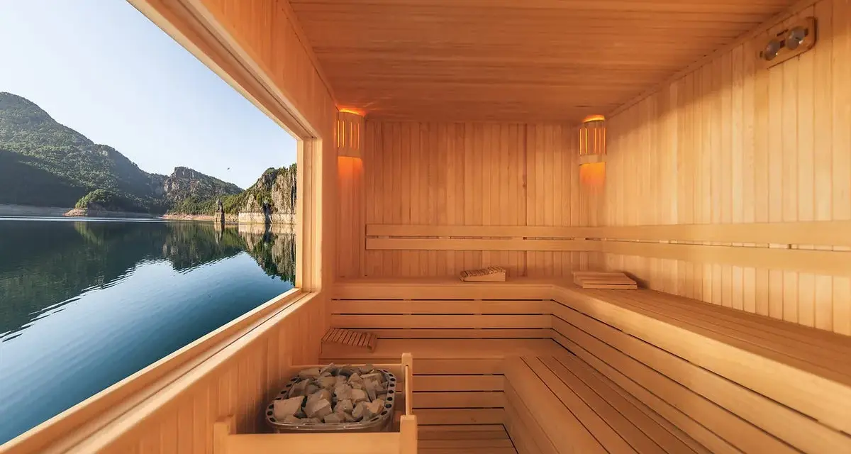 Interno di una sauna in legno con vista su un lago e montagne. Un luogo perfetto per capire cos'è una spa: relax e natura.