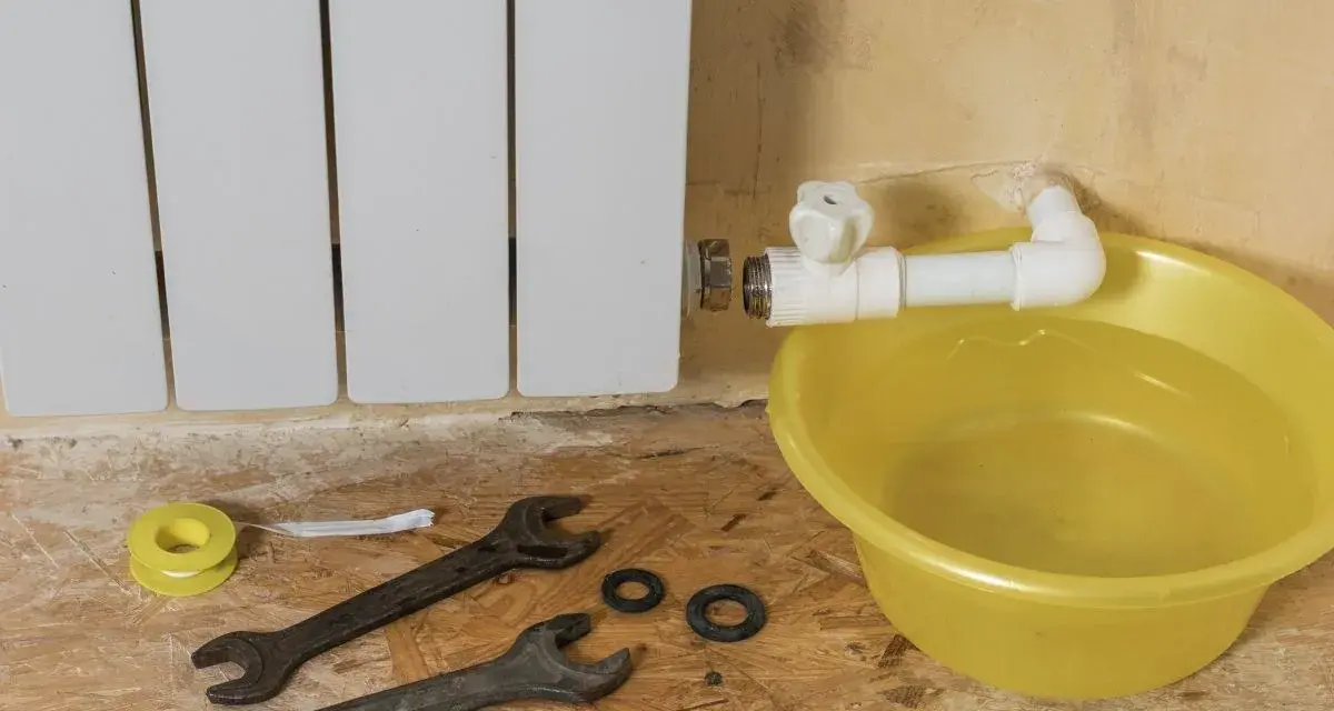 Riparazione di un termosifone che perde acqua e presenta ruggine. Attrezzi e bacinella gialla pronti per l'intervento.