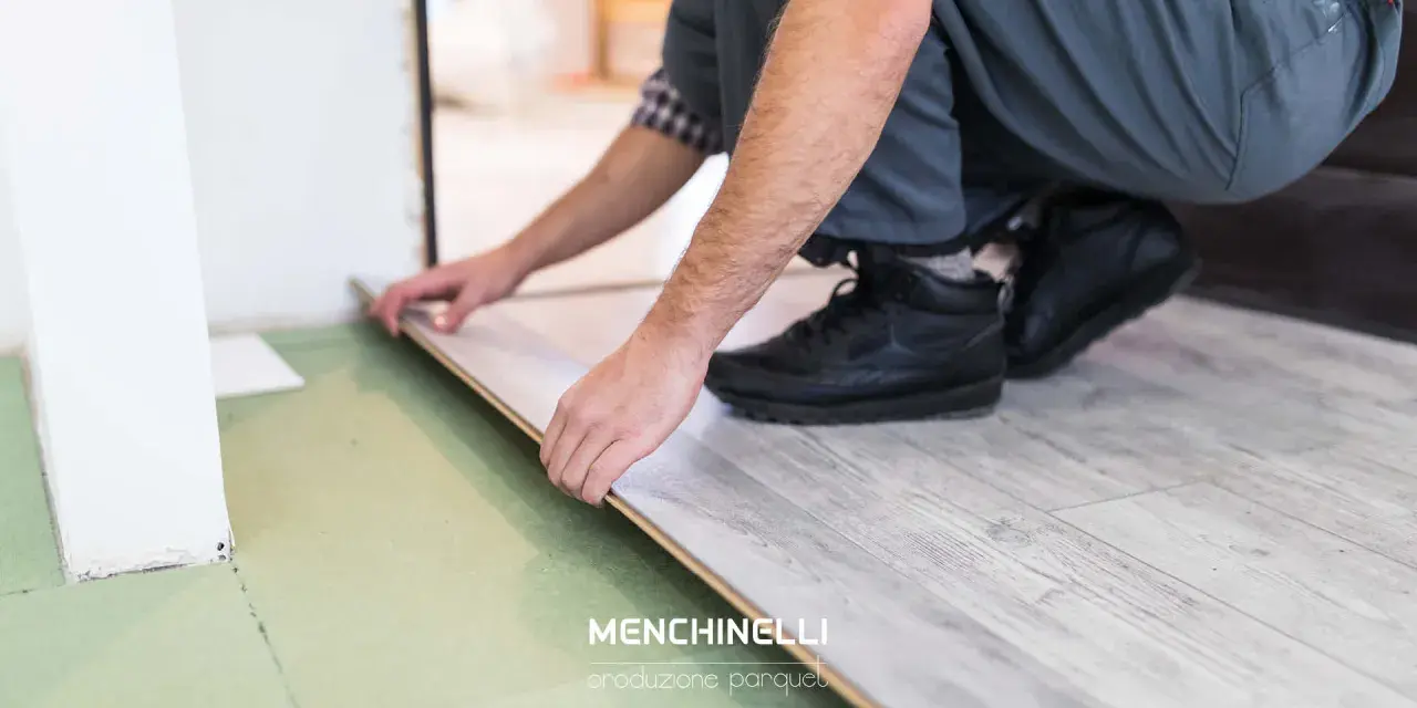 Installazione di un parquet flottante con finitura effetto legno chiaro. Un artigiano posa le tavole con cura.