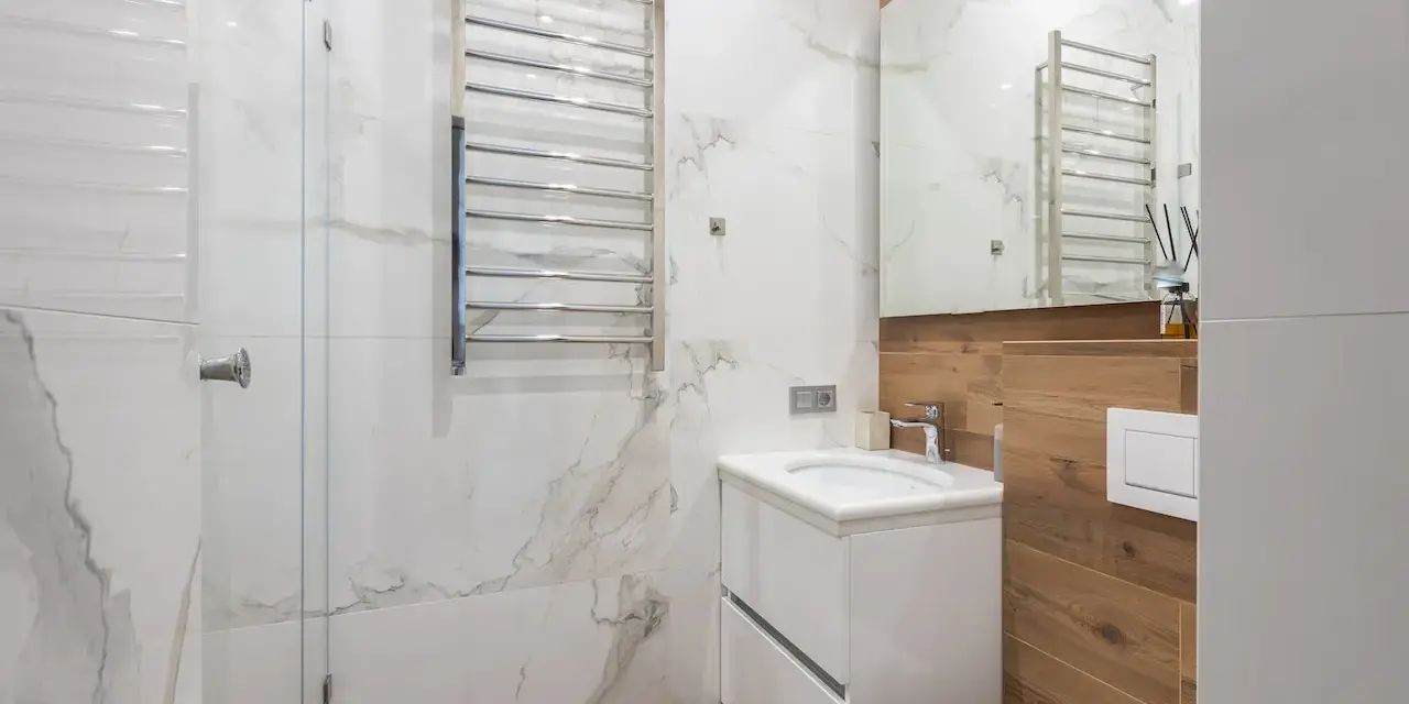 Bagno moderno con termoarredi cromati, lavabo sospeso e rivestimenti in marmo e legno.