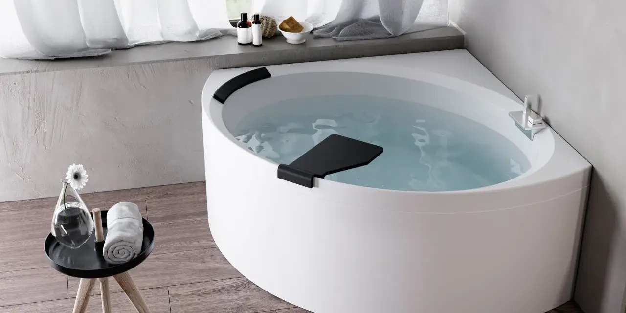 Una vasca da bagno angolare bianca, piena d'acqua, con accessori da bagno e un fiore su un tavolino. Un'esperienza novellini divina.
