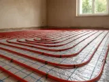 Sistema di riscaldamento a pavimento con tubi rossi disposti a spirale su una griglia blu. L'installazione è pronta per il massetto, garantendo un comfort termico ottimale.