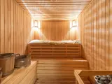 Interno di una sauna norvegese in legno, con panche, secchi e luci soffuse.
