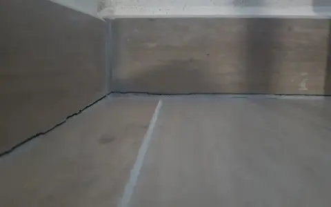 Angolo di una stanza con pavimento in legno e battiscopa. Si vedono le crepe tra il battiscopa e il muro, un dettaglio da considerare dopo il massetto.