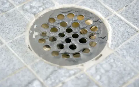Scarico doccia a pavimento con piastrelle grigie e acqua. La pendenza doccia a pavimento assicura il corretto deflusso.