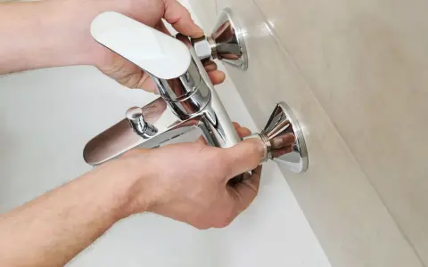 Mani che installano un nuovo miscelatore cromato per la vasca da bagno, parte della sostituzione miscelatore vasca da bagno.