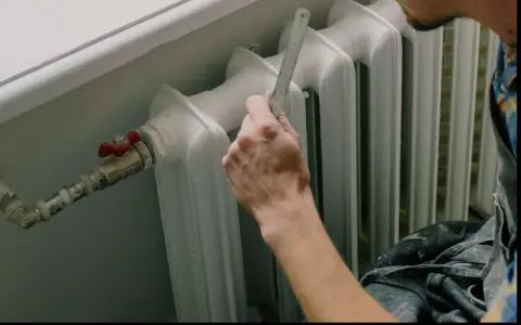 Mano con righello vicino a termosifone, pronto a cambiare valvola termostatica senza svuotare impianto.