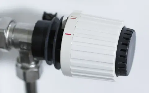 Dettaglio di un detentore termosifone con ghiera bianca e nera, impostato su una tacca intermedia, indica la regolazione della temperatura.