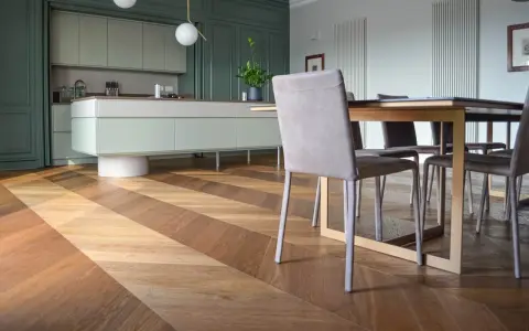 Un elegante parquet a spina di pesce crea un disegno dinamico sotto un tavolo da pranzo e una moderna cucina verde.