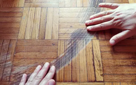 Mani sul parquet rovinato, mostrando graffi e usura. Si valuta come pulire e ripristinare il legno.