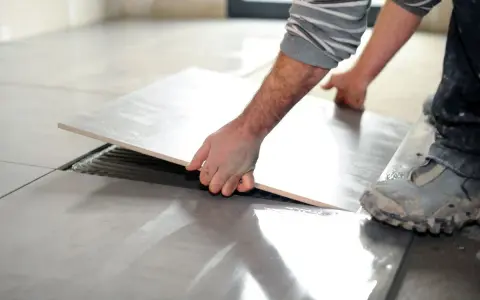 Mano che solleva una piastrella per rimuovere pavimento sovrapposto. Lavori di ristrutturazione in corso.