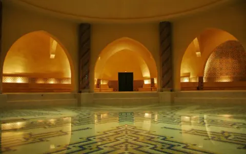 Interno di un bagno dei turchi con piscina e mosaici geometrici. Archi moreschi e colonne decorate creano un'atmosfera orientale.