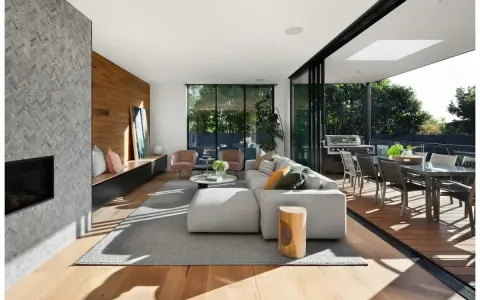 Soggiorno moderno con camino in pietra, divano bianco, e un bellissimo parquet essenze che si estende verso l'esterno, collegandosi alla zona pranzo esterna.