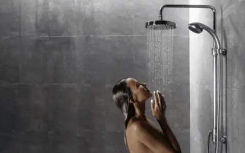 Donna sotto una doccia walk in dimensioni ideali, con le mani giunte sotto il getto d'acqua.