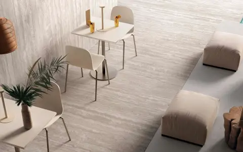 Un'area lounge moderna con tavolini, sedie e pouf su eleganti mattonelle senza fuga effetto pietra.