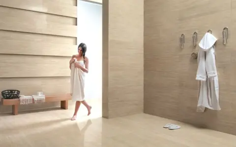 Bagni moderni con donna avvolta in un asciugamano, accappatoio appeso e panchina in legno.