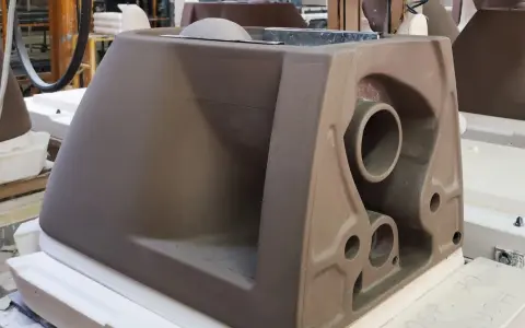 A brown ceramic toilet tank mold with visible pipes and openings, in a workshop setting.
