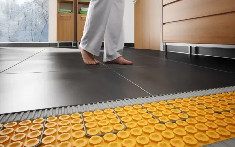 Piedi nudi su pavimento scuro, con sistema di riscaldamento a pavimento su pavimento esistente visibile sotto.