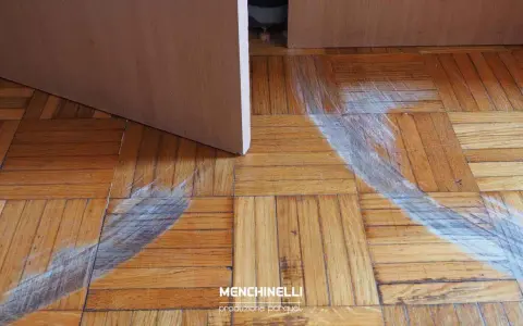 Rimozione di parquet incollato con segni di usura sul pavimento in legno.