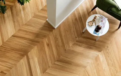 Un elegante parquet oliato a spina di pesce, con un tavolino bianco e una poltrona verde. Scopri come pulire il tuo parquet oliato per mantenerlo splendente.