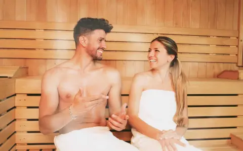 Coppia sorridente in una sauna di legno, un rituale di benessere quotidiano.