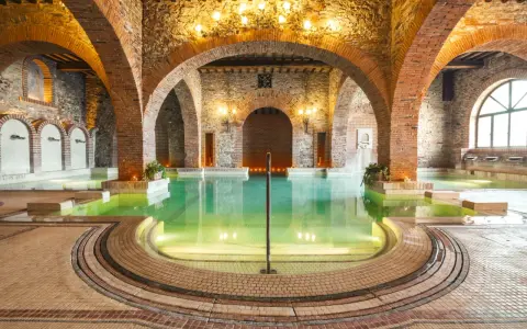 Un suggestivo thermarium, con vasche termali verdi sotto archi in mattoni e pietra, evoca un'atmosfera di antico benessere.