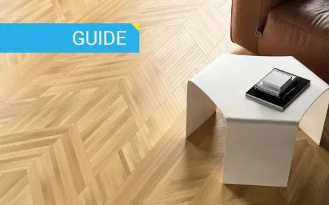Guida: parquet spazzolato pro e contro. Pavimento in legno con motivo a spina di pesce, tavolino bianco e divano in pelle marrone.