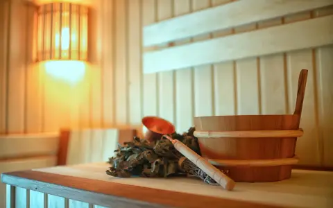 Un secchio di legno, un mestolo di rame e un fascio di rami per la sauna casalinga, illuminati da una luce calda.