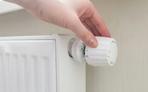 Mano che regola la manopola di un termosifone per ottimizzare la potenza.