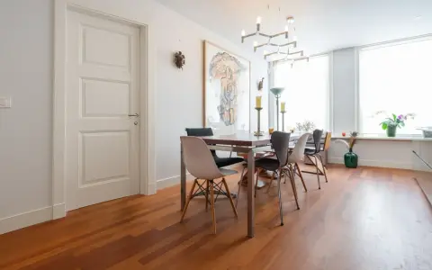 Un elegante soggiorno con parquet doussié e arredamento moderno. Tavolo da pranzo con sedie di design, quadro astratto e lampadario geometrico.