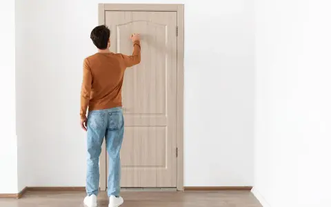Uomo con maglione arancione e jeans bussa alla porta, forse per alzare la porta per posa pavimento.