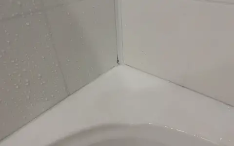 Angolo di una vasca da bagno con piastrelle bagnate e un sigillante bianco appena applicato per sigillare la vasca da bagno.