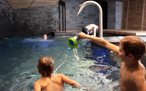 Bambini giocano in piscina, con un annaffiatoio. Nessuna indicazione su sauna età minima.