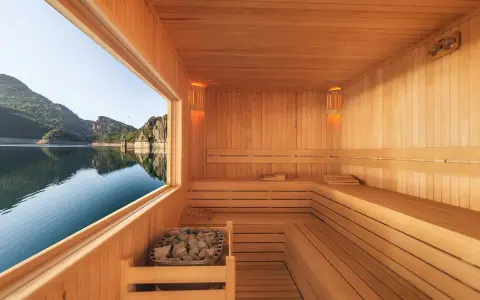 Interno di una sauna in legno con vista su un lago e montagne. Un luogo perfetto per capire cos'è una spa: relax e natura.