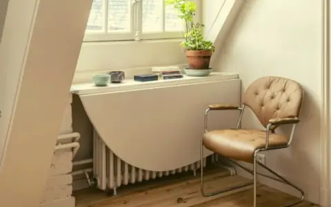Angolo studio con sedia in pelle e un tavolo ribaltabile che nasconde un termosifone. Ricorda: non coprire i termosifoni per un riscaldamento efficiente.