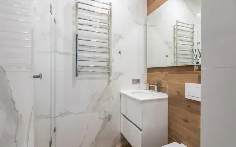 Bagno moderno con termoarredi cromati, lavabo sospeso e rivestimenti in marmo e legno.