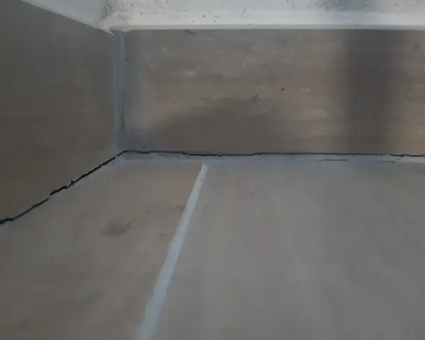 Angolo di una stanza con pavimento in legno e battiscopa. Si vedono le crepe tra il battiscopa e il muro, un dettaglio da considerare dopo il massetto.