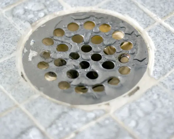 Scarico doccia a pavimento con piastrelle grigie e acqua. La pendenza doccia a pavimento assicura il corretto deflusso.