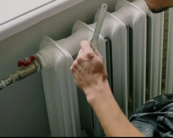 Mano con righello vicino a termosifone, pronto a cambiare valvola termostatica senza svuotare impianto.