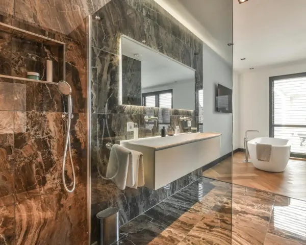 Bagno di lusso con doccia e vasca. Rubinetteria Bossini cromata, lavabo sospeso e specchio illuminato. Marmo scuro e parquet.