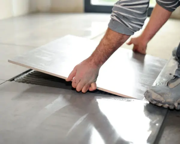 Mano che solleva una piastrella per rimuovere pavimento sovrapposto. Lavori di ristrutturazione in corso.